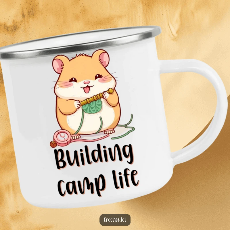 Funny camping mug with a plump, cheerful hamster character building a small structure with a crochet hook, ideal for outdoor enjoyment.