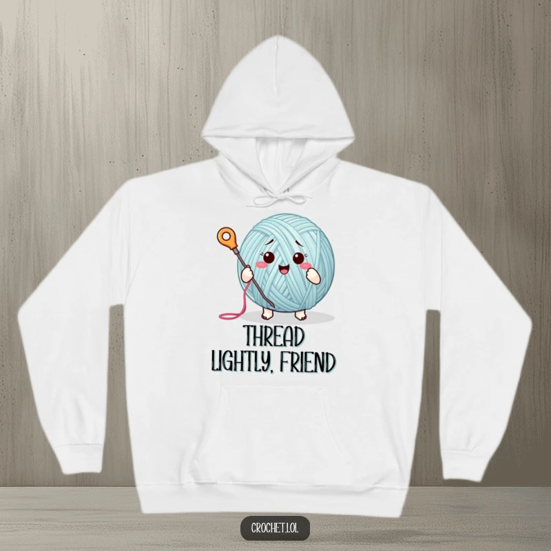 Funny hoodie with a happy yarn ball character gleefully stitching using a needle and thread, ideal for cozy crafting.